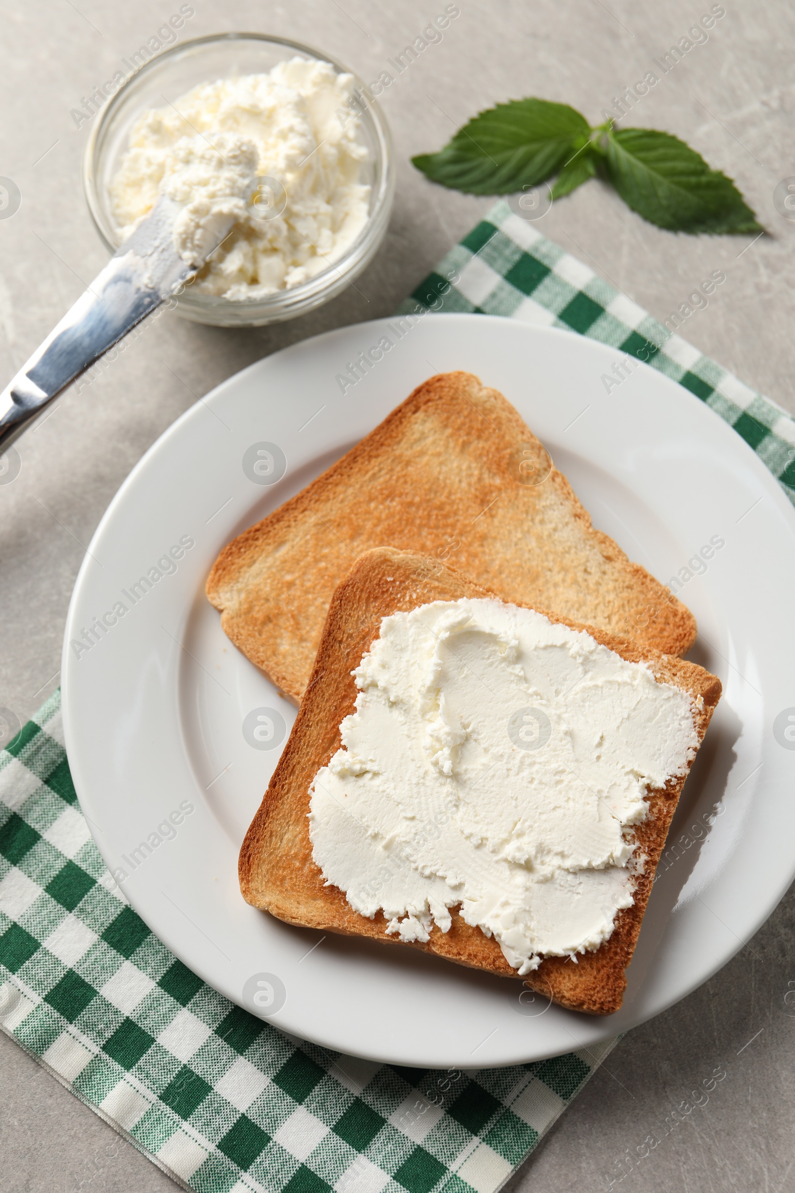 Photo of Delicious toasted bread slices with cream cheese, mint and knife on grey textured table, flat lay