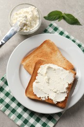 Delicious toasted bread slices with cream cheese, mint and knife on grey textured table, flat lay