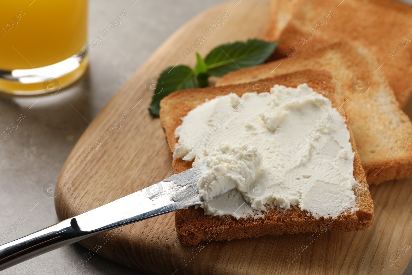 Photo of Delicious toasted bread slices with cream cheese and knife on grey table, closeup