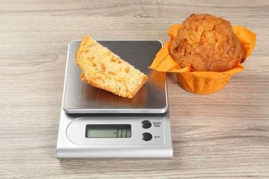 Kitchen scale with piece of muffin on light wooden table, closeup