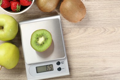 Kitchen scale with piece of kiwi, apples and strawberries on light wooden table, flat lay. Space for text