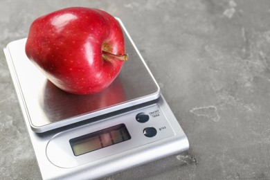 Kitchen scale with apple on grey textured table, closeup. Space for text