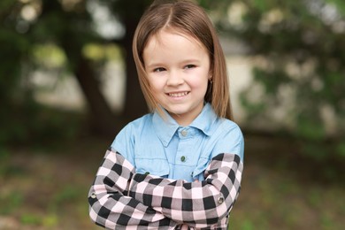 Photo of Portrait of happy little girl with crossed arms outdoors