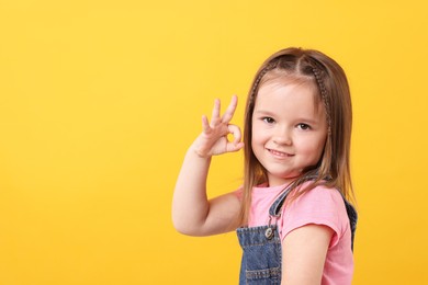 Photo of Portrait of cute little girl showing OK gesture on orange background, space for text