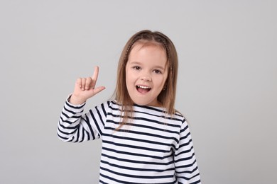 Portrait of emotional little girl pointing at something on grey background