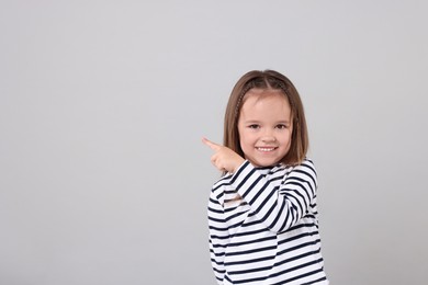 Photo of Portrait of happy little girl pointing at something on grey background, space for text