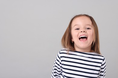 Portrait of emotional little girl on grey background, space for text