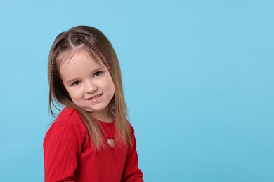 Portrait of cute little girl on light blue background, space for text