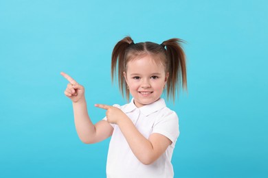 Photo of Portrait of happy little girl pointing at something on light blue background