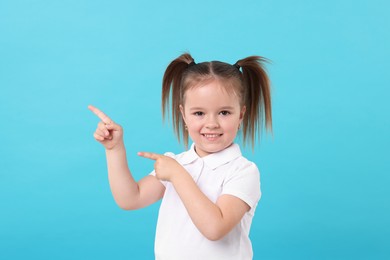 Portrait of happy little girl pointing at something on light blue background