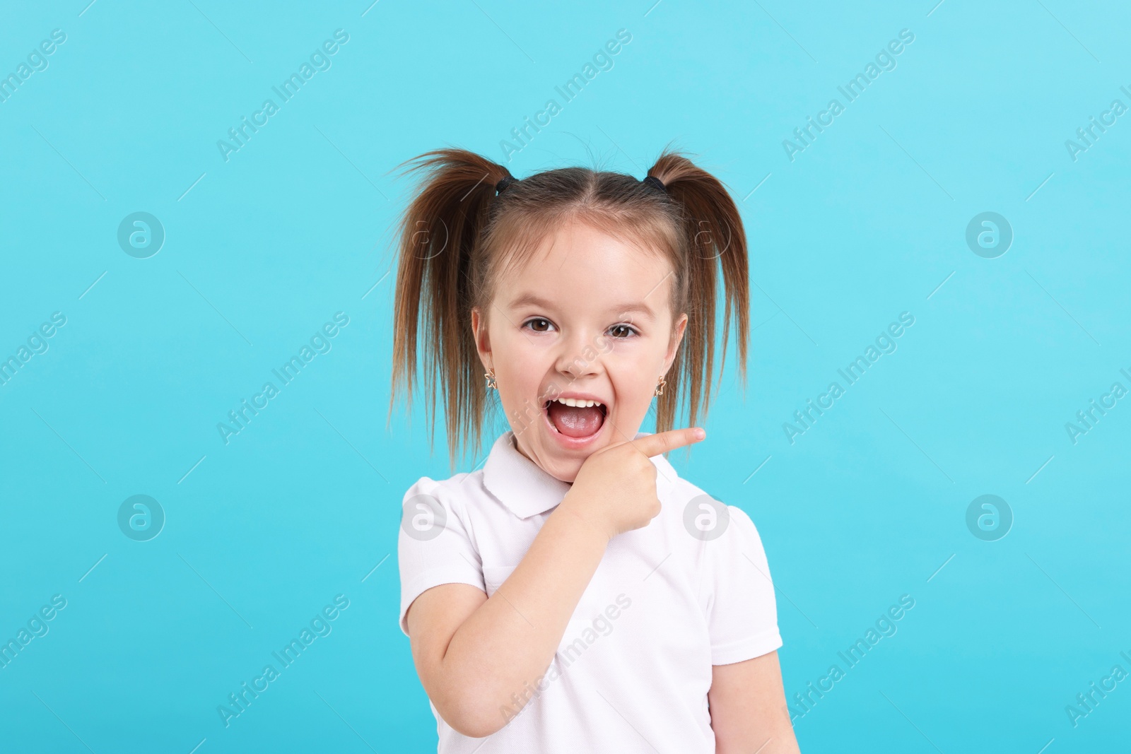 Photo of Portrait of emotional little girl pointing at something on light blue background