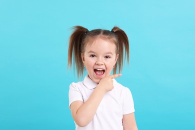 Photo of Portrait of emotional little girl pointing at something on light blue background