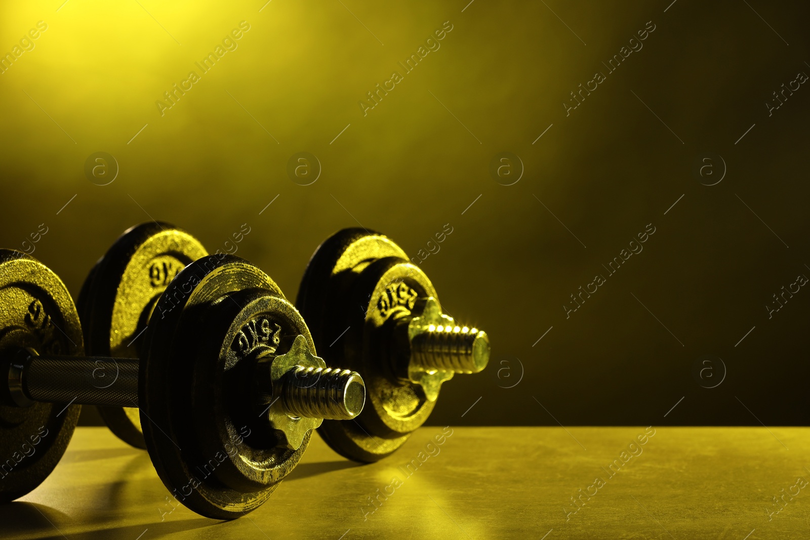 Photo of Two barbells on table in color lights. Space for text