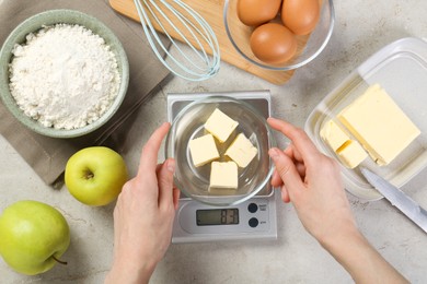 Photo of Woman weighing butter on kitchen scale at grey table, top view