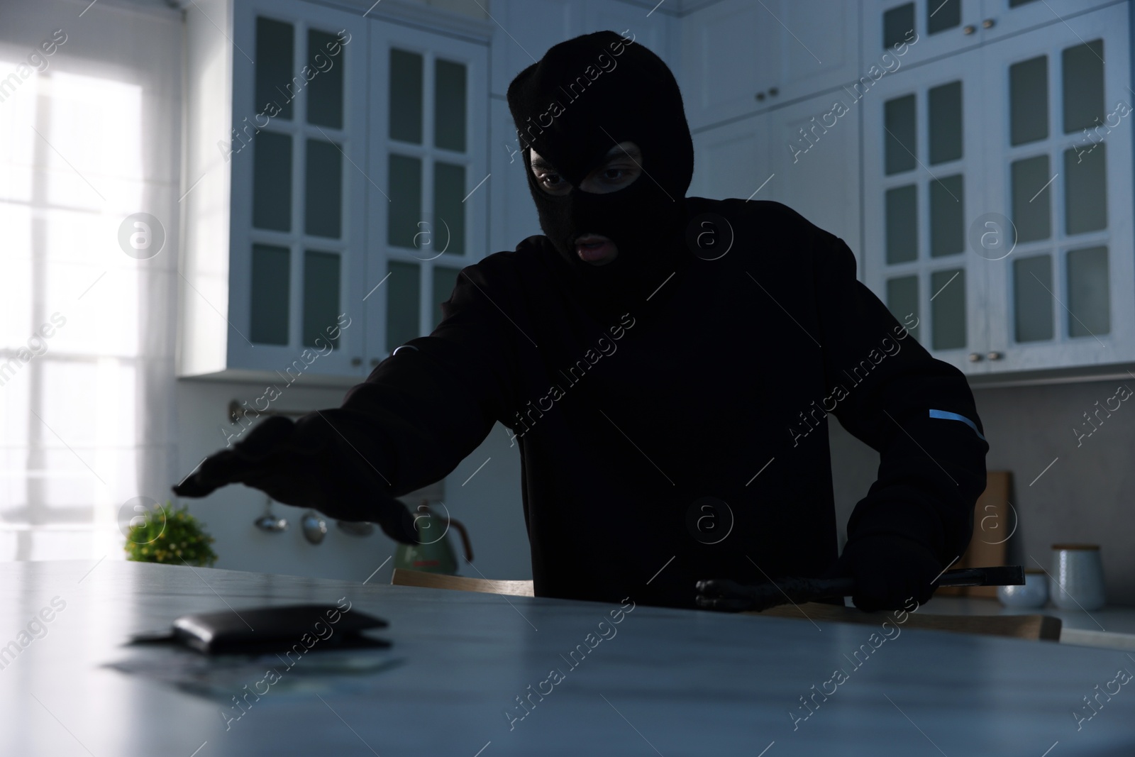 Photo of Thief wearing balaclava stealing wallet with money in foreign house, low angle view. Burglary