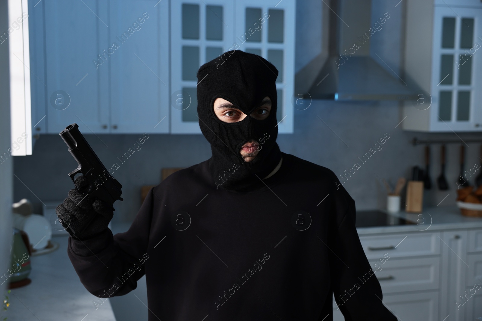 Photo of Thief wearing balaclava with gun in foreign house. Burglary