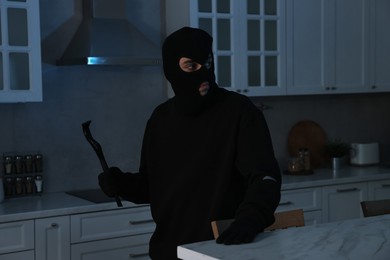 Photo of Thief wearing balaclava with crowbar in foreign house. Burglary