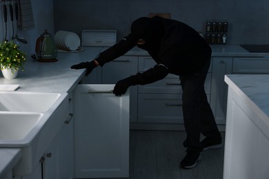 Thief wearing balaclava looking into cupboard in foreign house. Burglary