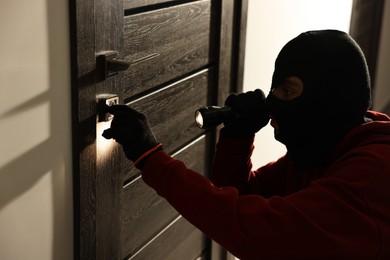 Thief with flashlight breaking foreign door's lock in hall. Burglary