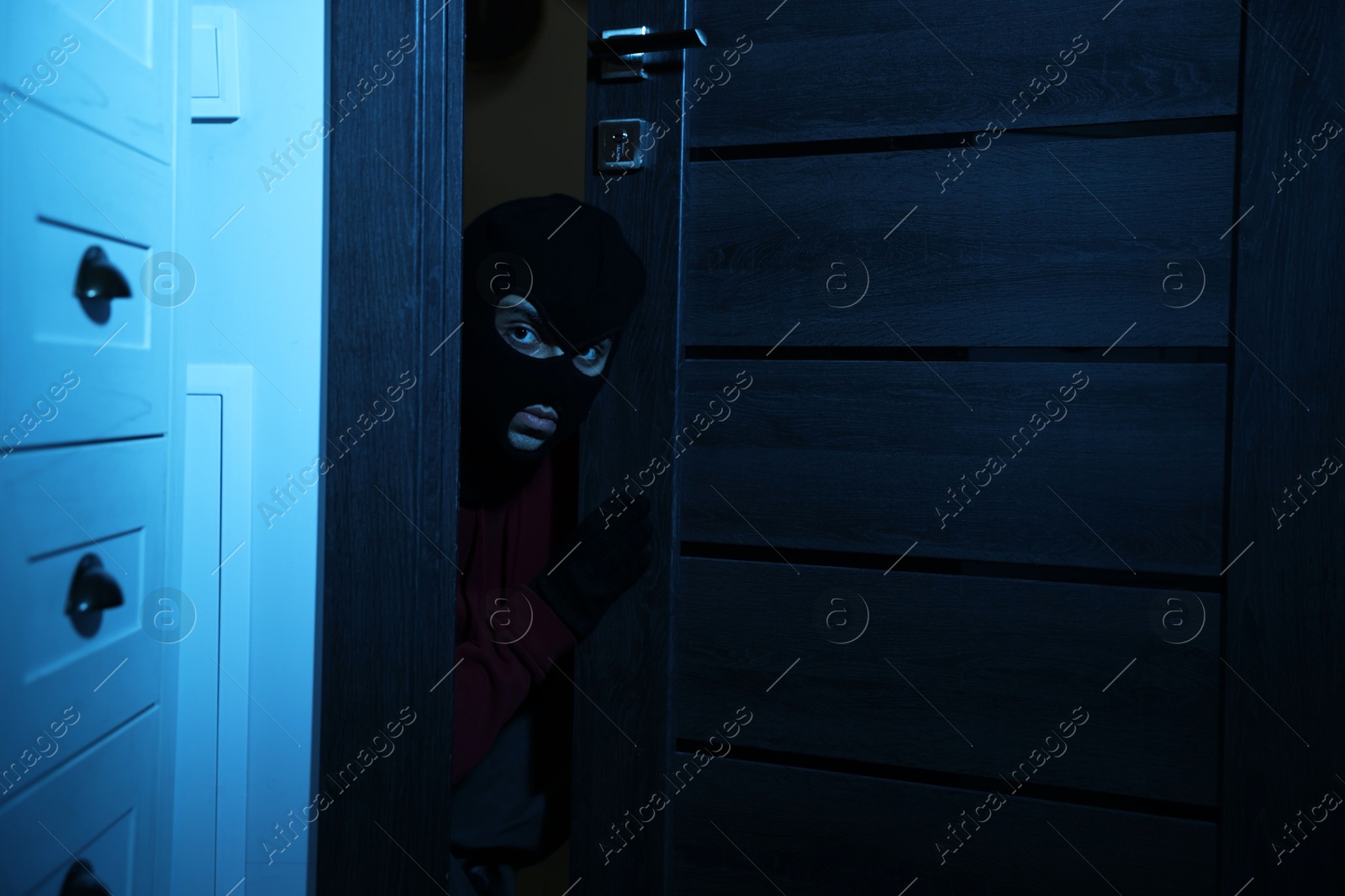 Photo of Thief in balaclava entering foreign house at night. Burglary