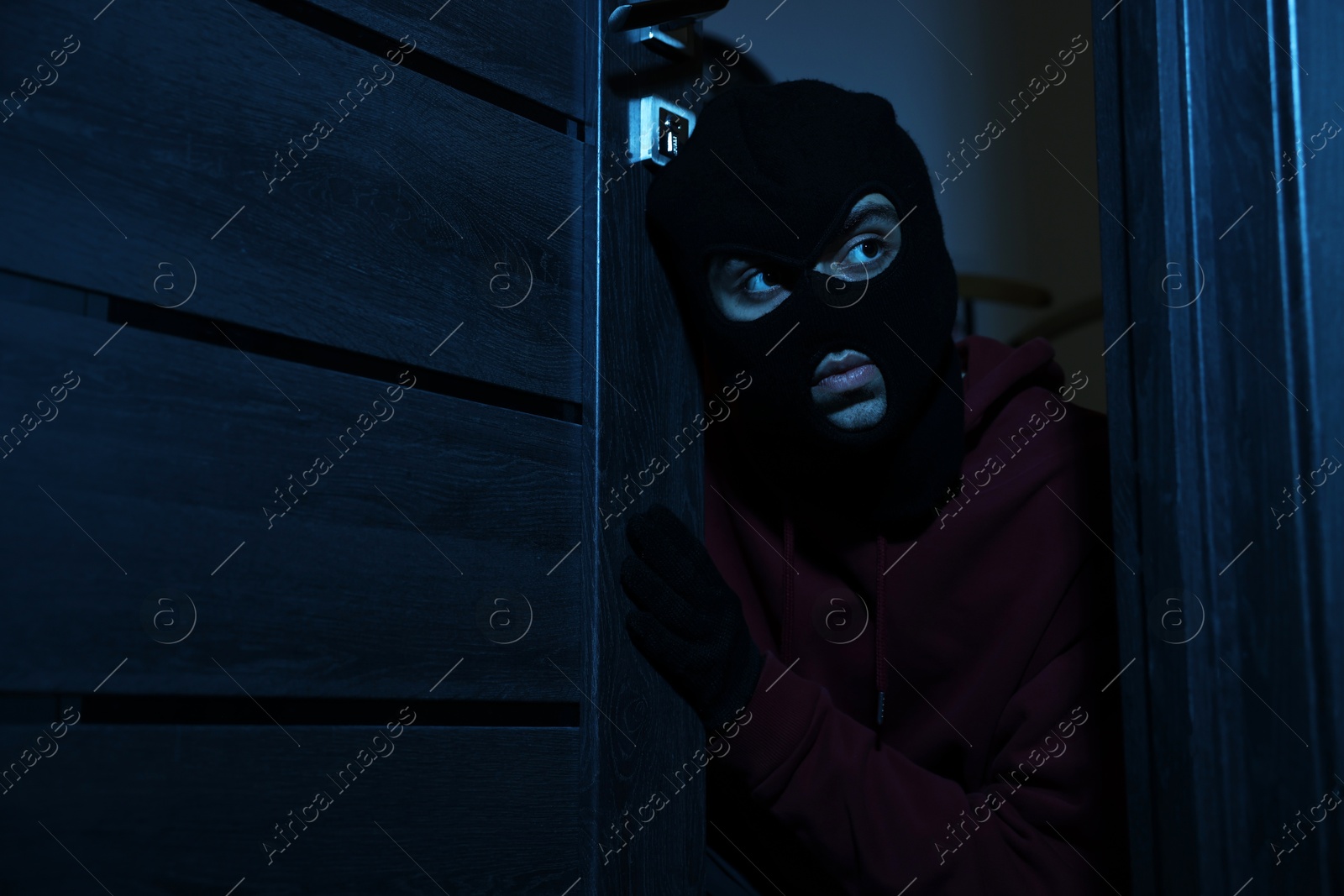 Photo of Thief in balaclava entering foreign house at night. Burglary