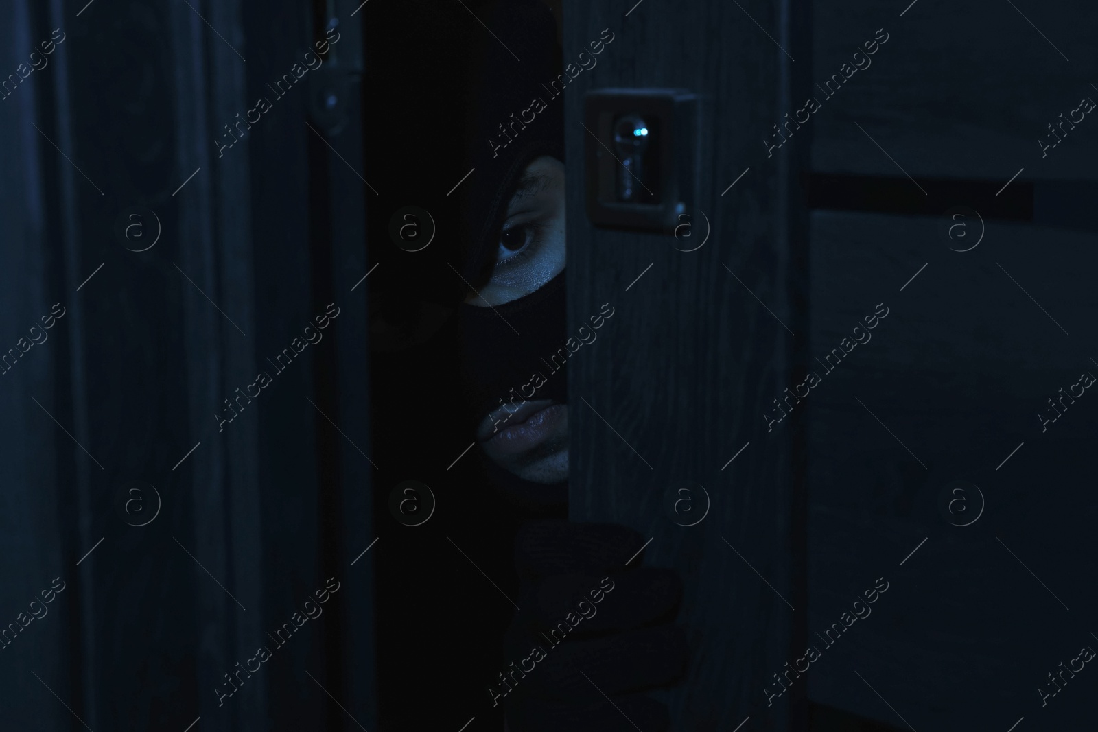 Photo of Thief in balaclava entering foreign house at night. Burglary