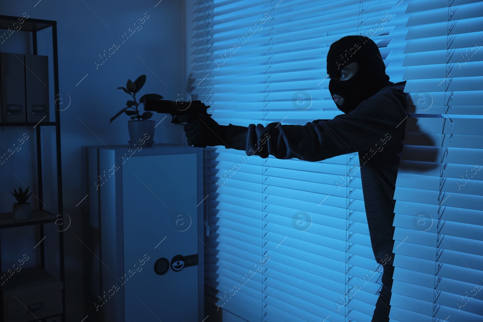 Photo of Thief with gun coming out of blinds at night. Burglary