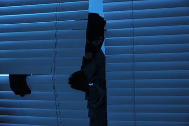 Photo of Thief looking out of blinds at night. Burglary