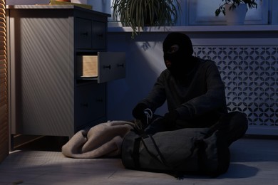 Photo of Thief wearing balaclava stealing jewels in foreign house. Burglary