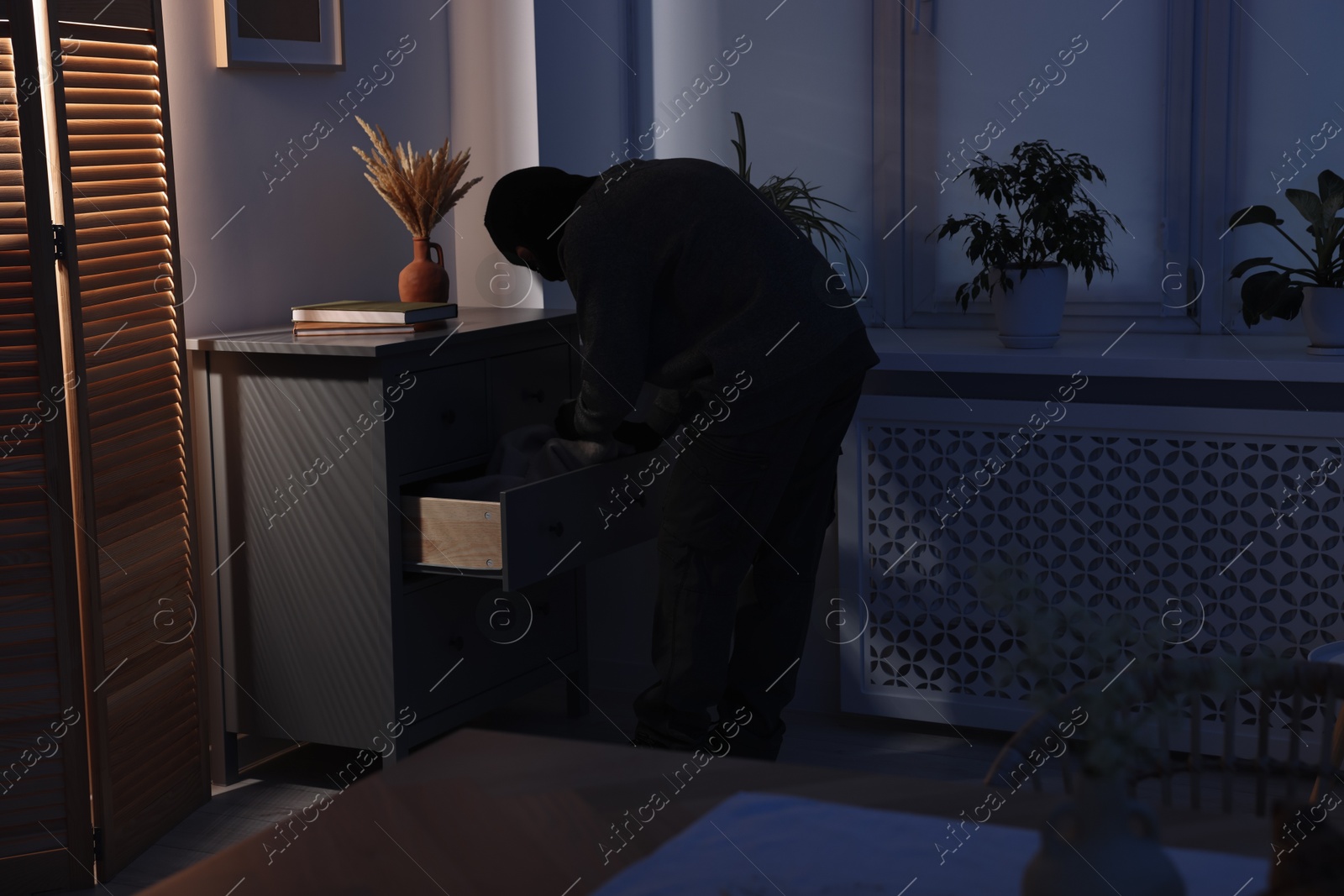 Photo of Thief wearing balaclava looking for money in foreign house. Burglary