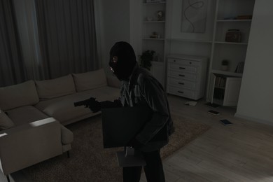 Photo of Thief with gun stealing computer monitor at foreign house. Burglary