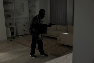 Photo of Thief with gun stealing computer monitor at foreign house. Burglary