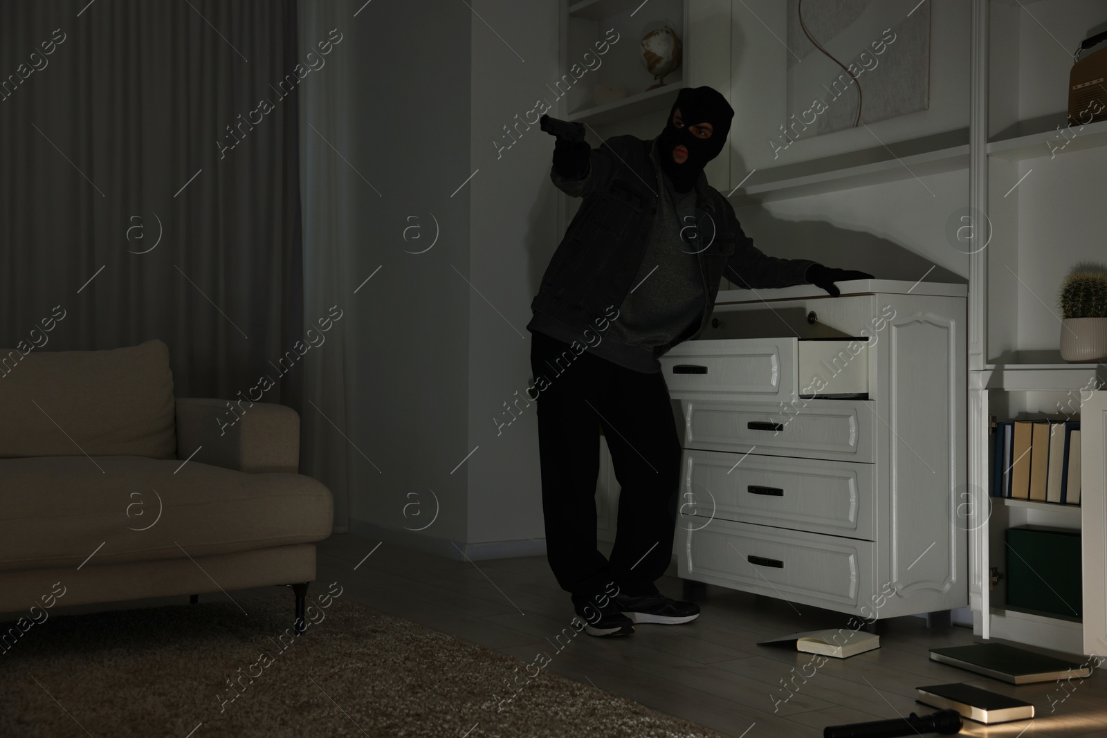 Photo of Thief with gun near chest of drawers at foreign house, low angle view. Burglary