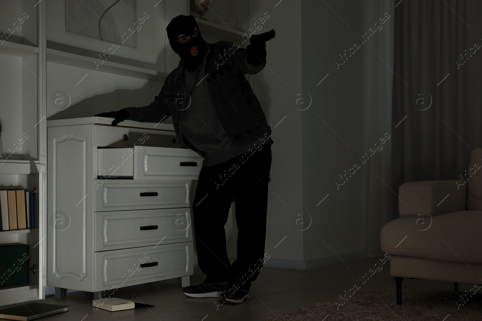 Photo of Thief with gun near chest of drawers at foreign house, low angle view. Burglary