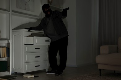 Thief with gun near chest of drawers at foreign house, low angle view. Burglary