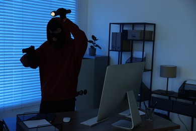 Photo of Thief with flashlight and gun in office at night. Burglary