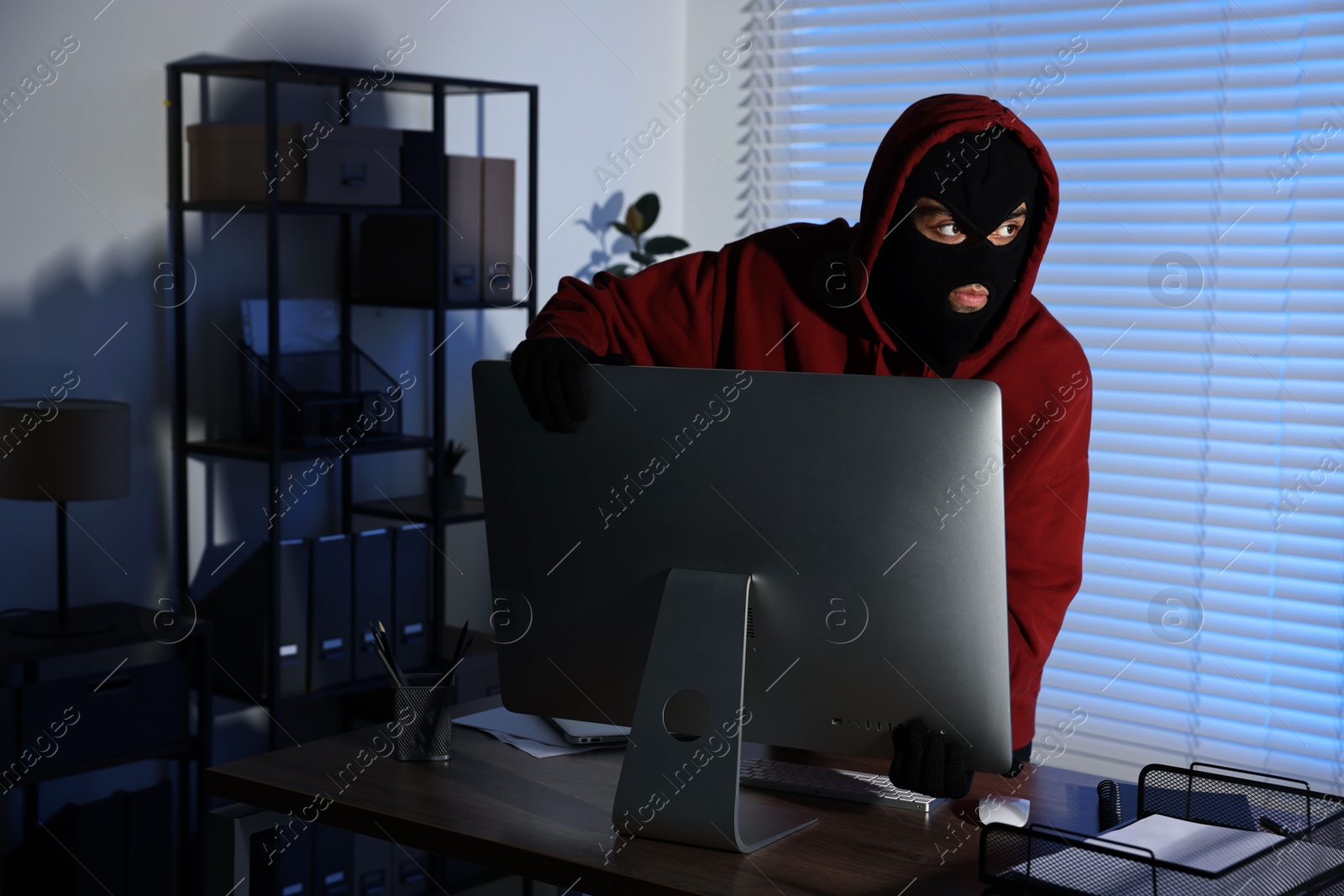 Photo of Thief stealing computer monitor in office at night. Burglary