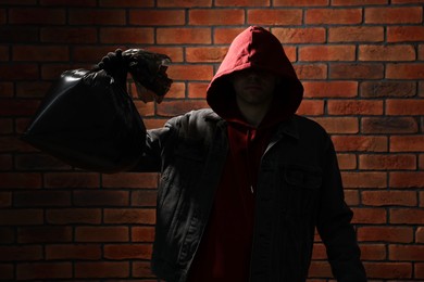 Photo of Thief in hoodie with bag against red brick wall