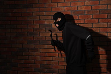 Photo of Thief in balaclava with crowbar against red brick wall. Space for text