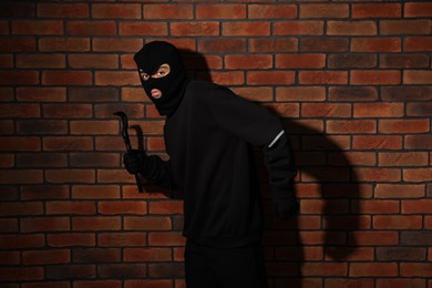 Photo of Thief in balaclava with crowbar against red brick wall