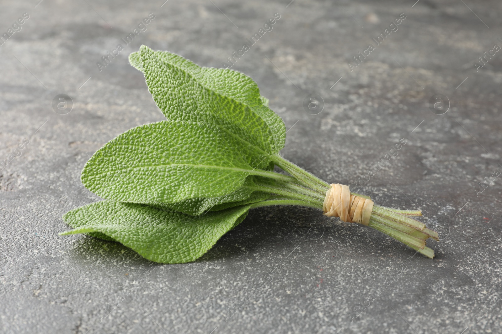 Photo of Bunch of green sage leaves on grey textured table, closeup