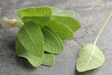 Photo of Bunch of green sage leaves on grey textured table, closeup