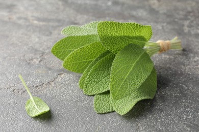 Photo of Bunch of green sage leaves on grey textured table, closeup