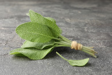 Photo of Bunch of green sage leaves on grey textured table, closeup