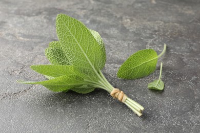 Photo of Bunch of green sage leaves on grey textured table, closeup