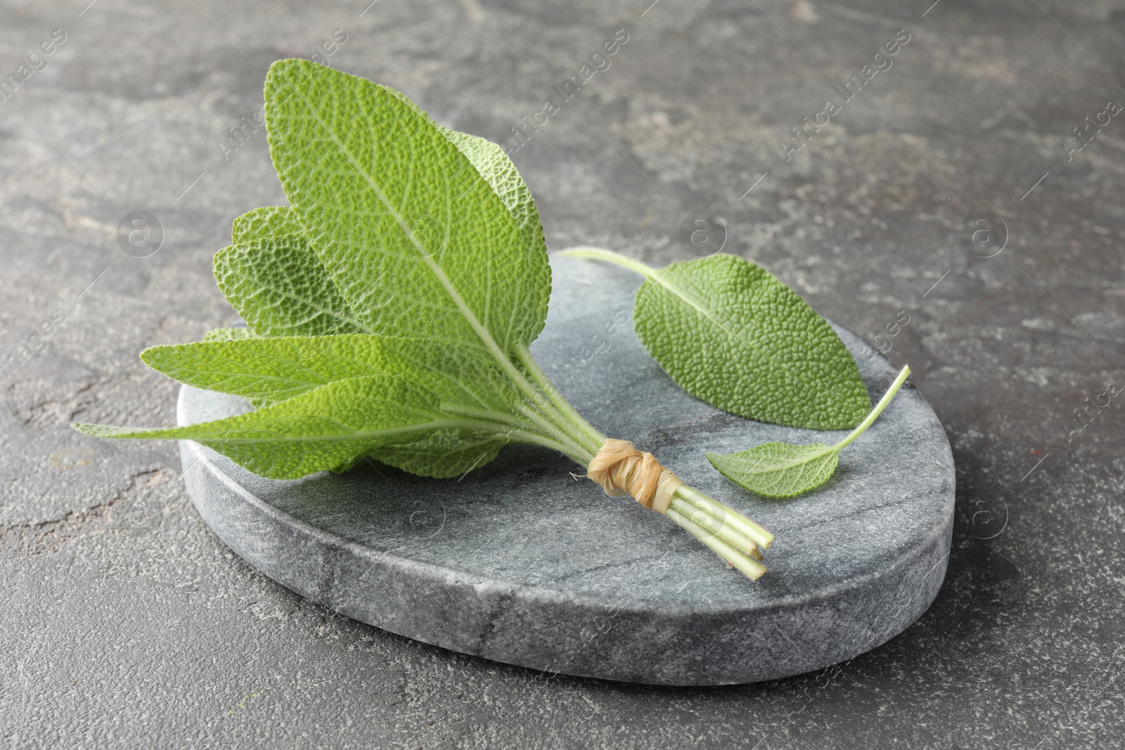 Photo of Bunch of green sage leaves on grey textured table, closeup