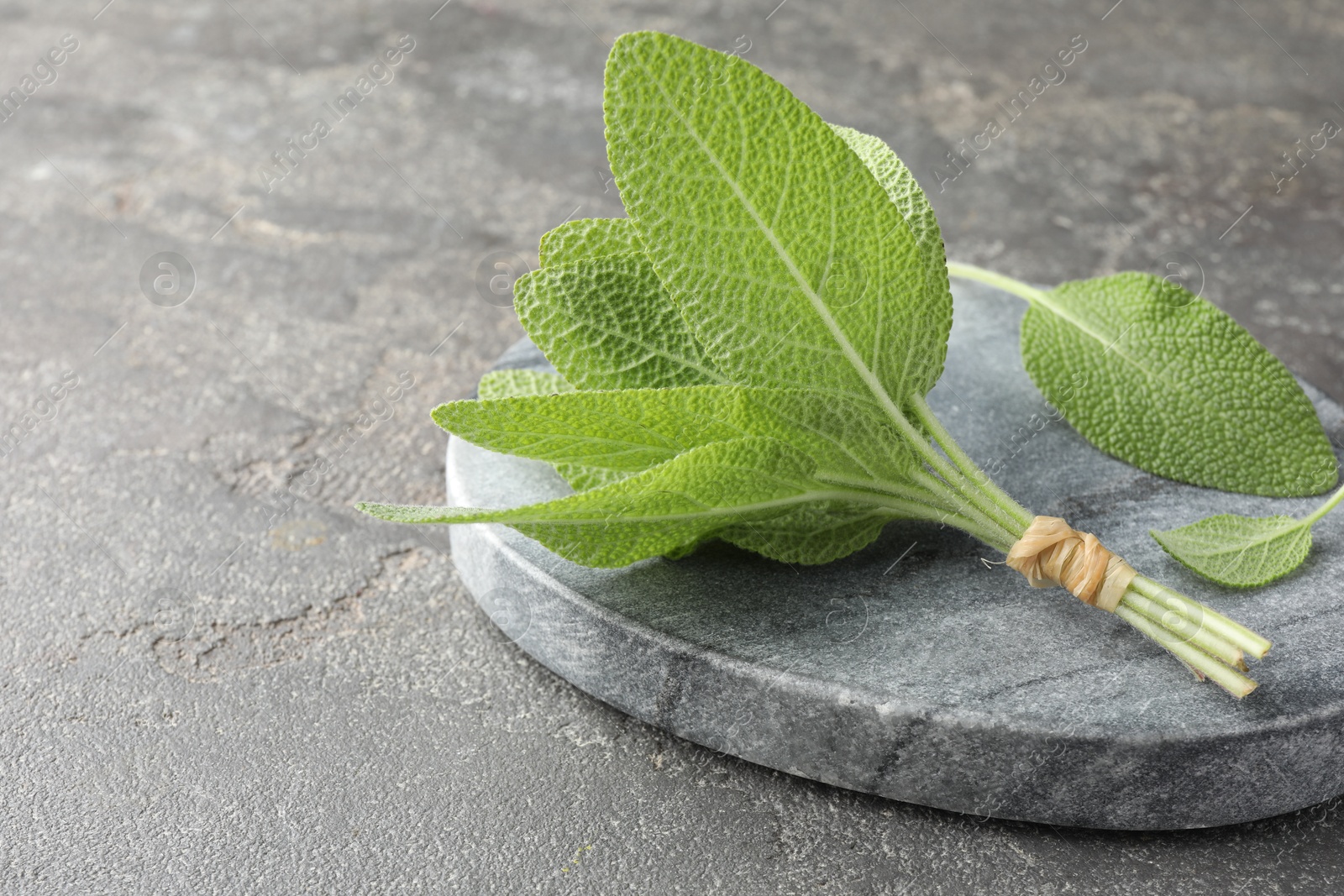 Photo of Bunch of green sage leaves on grey textured table, closeup. Space for text