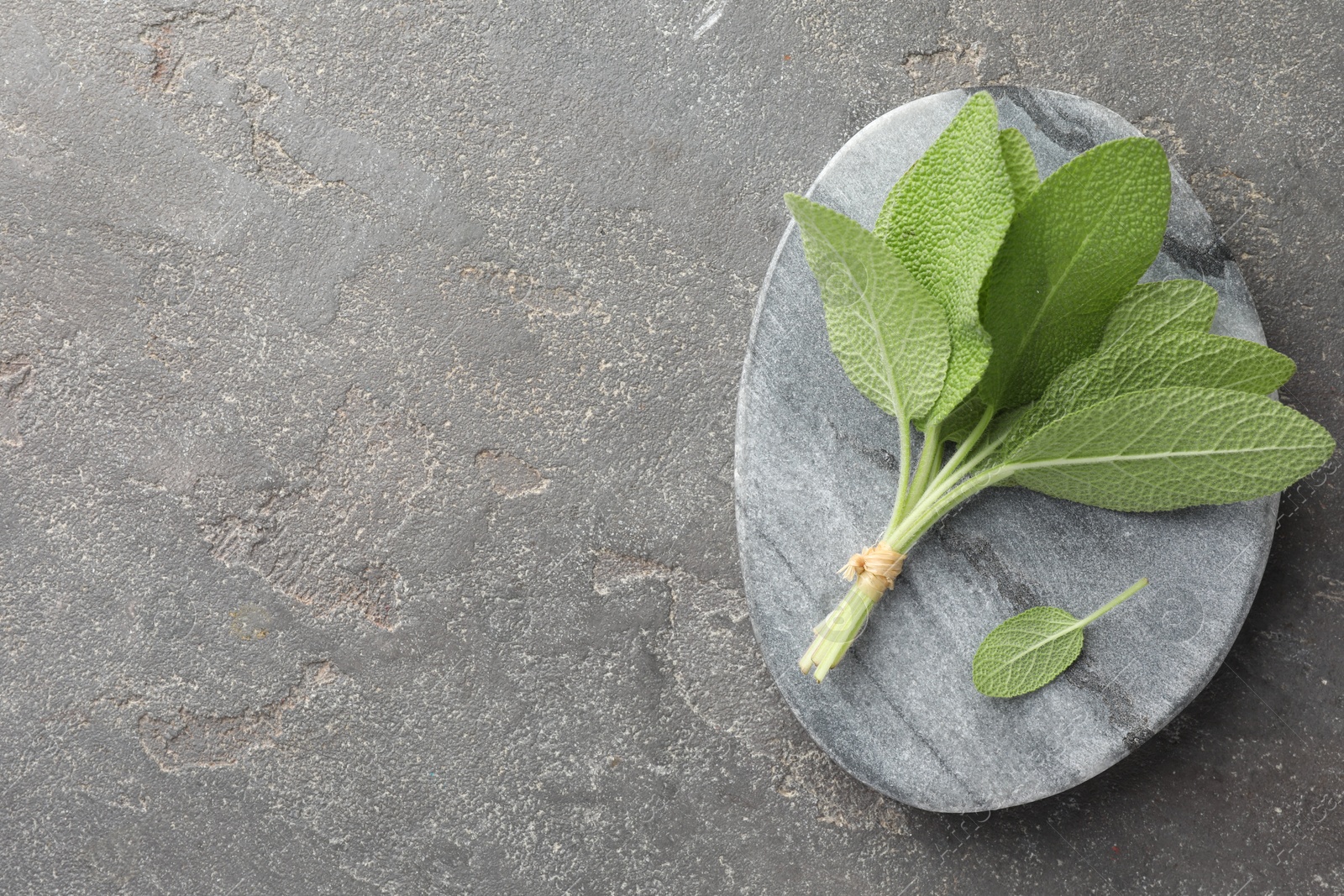 Photo of Bunch of green sage leaves on grey textured table, top view. Space for text