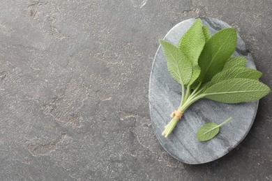 Photo of Bunch of green sage leaves on grey textured table, top view. Space for text