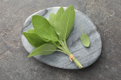 Photo of Bunch of green sage leaves on grey textured table, top view